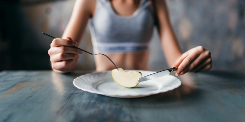 Female person against plate with a slice of apple. Weight loss diet concept