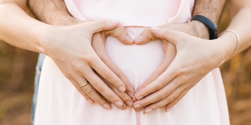 The future father hugs the belly of a pregnant woman, the expectant mother and makes hands with her in the form of a heart. Care and love for the child